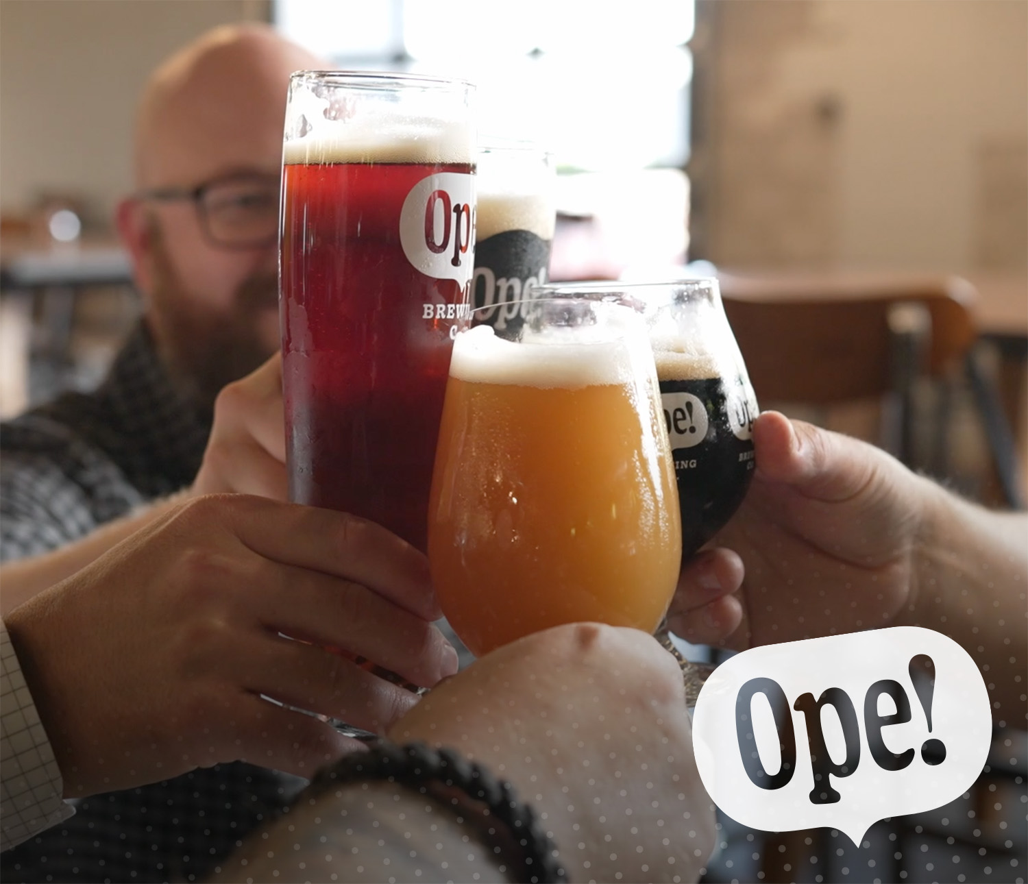 a group of hands clinking Ope Brewery glasses at the middle of a table